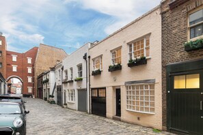 Een smalle straat met keien, omzoomd door traditionele gebouwen met gevels van baksteen en pleisterwerk, waarvan sommigen bloembakken en grote ramen hebben.