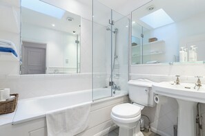 Een moderne badkamer met een douchecabine van glas, een witte badkuip, toilet en wastafel.