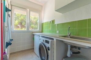 Eine kleine Küche mit Waschmaschine, Spüle und einem Fenster mit Jalousien.
