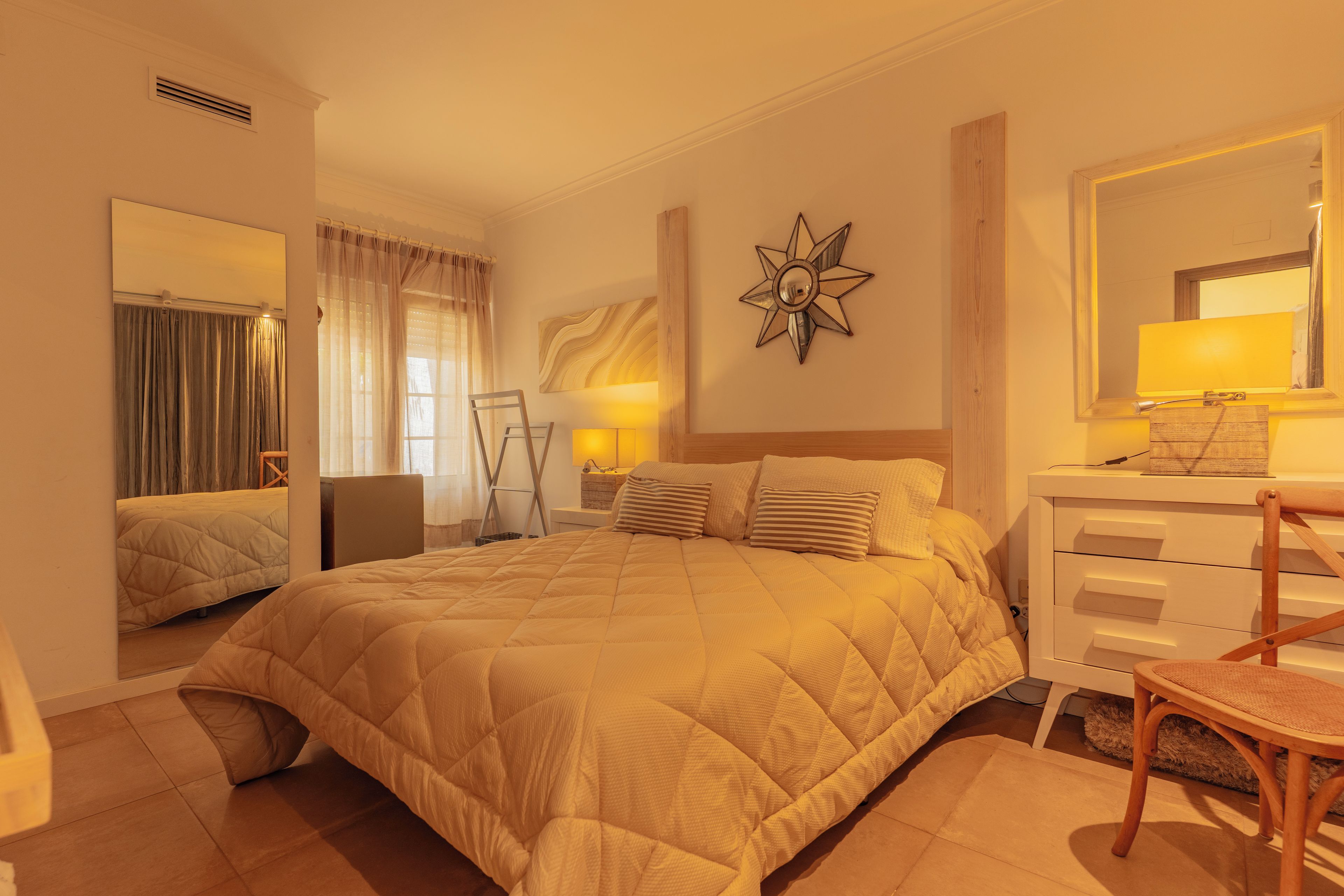 A hotel room with a large bed, a bedside table with a lamp, a chair, and a dresser.