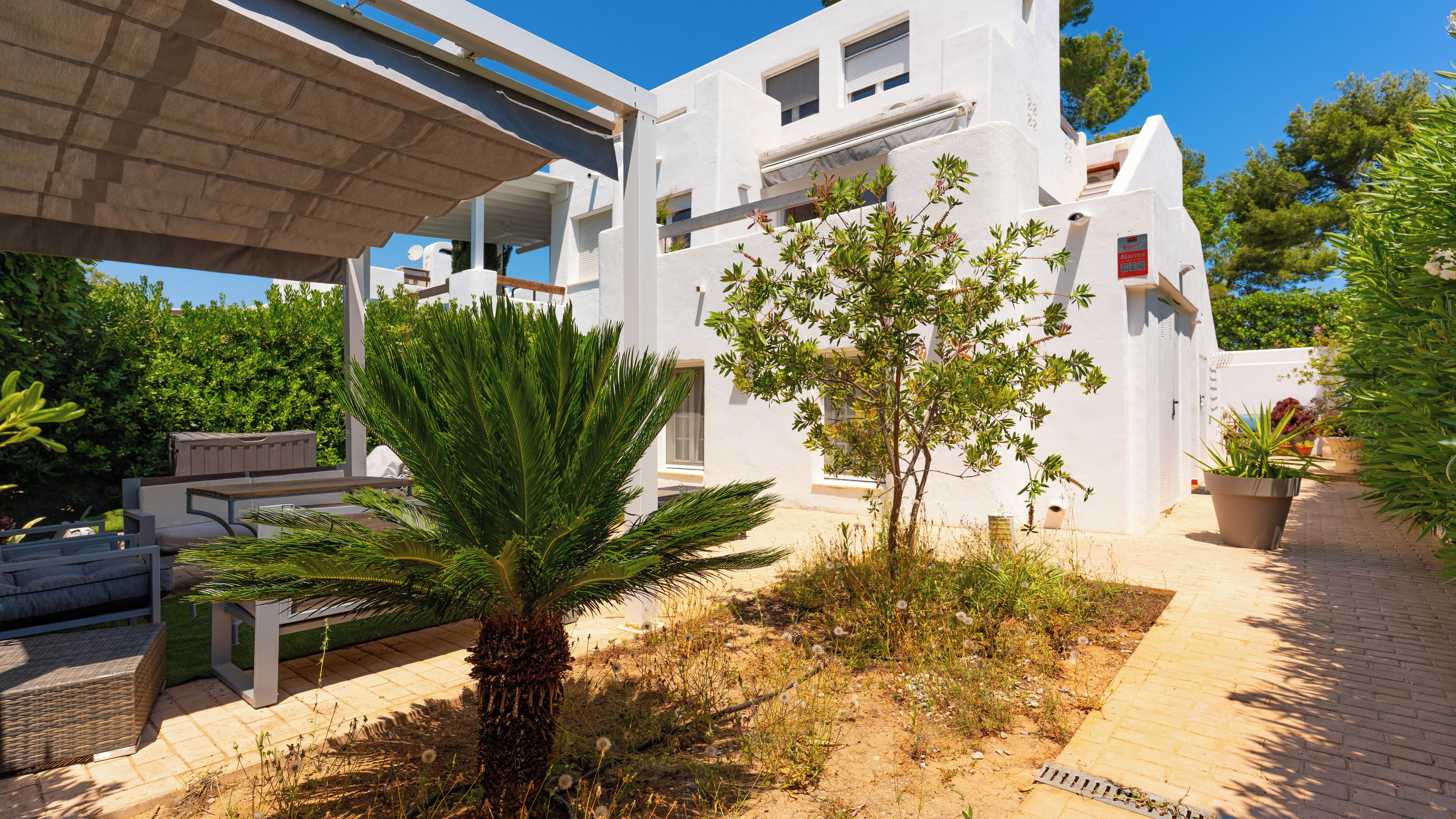A white building with a covered patio area, outdoor seating, and potted plants.
