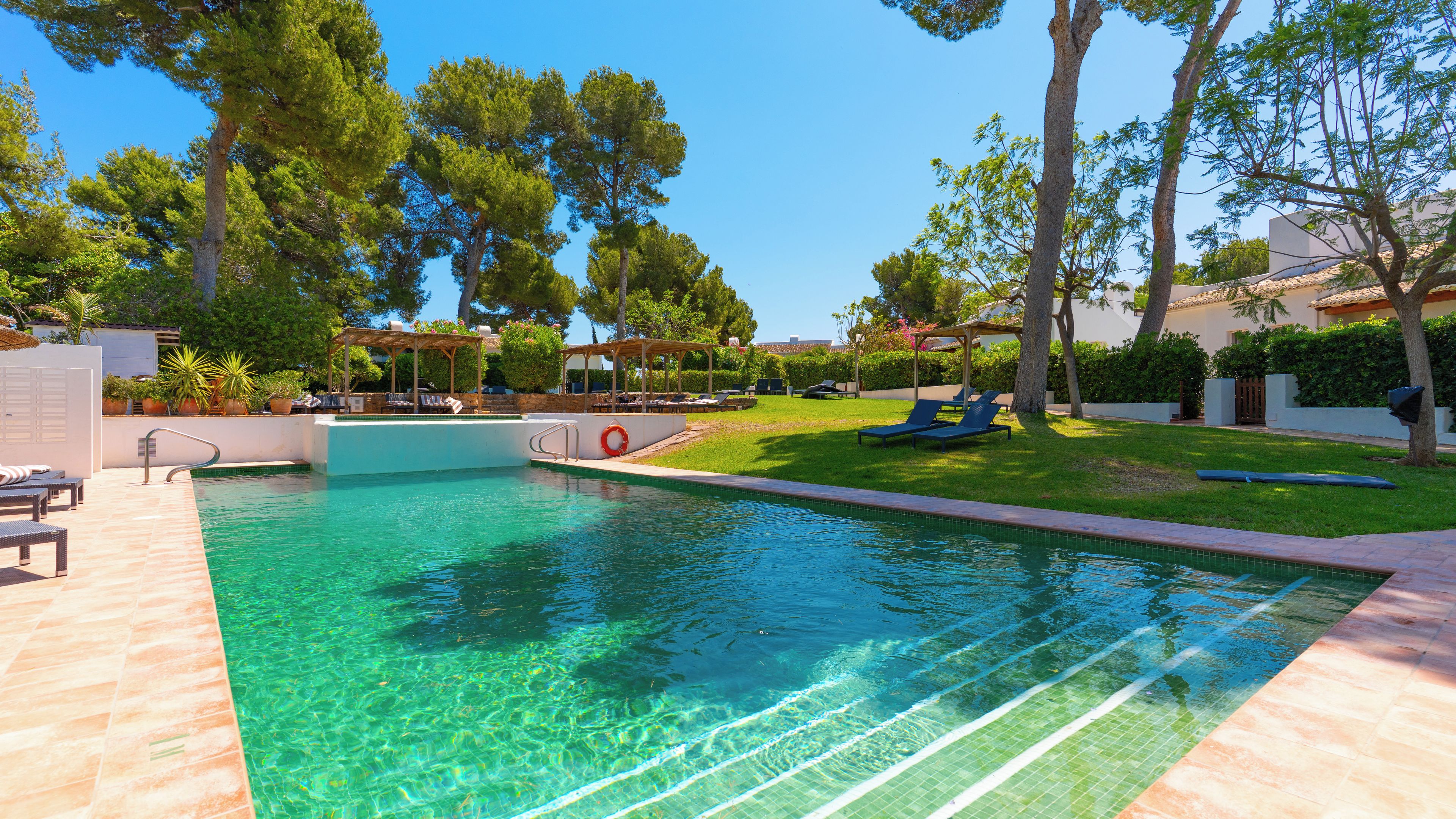 A swimming pool with clear water, surrounded by a patio area with lounge chairs and a pergola.