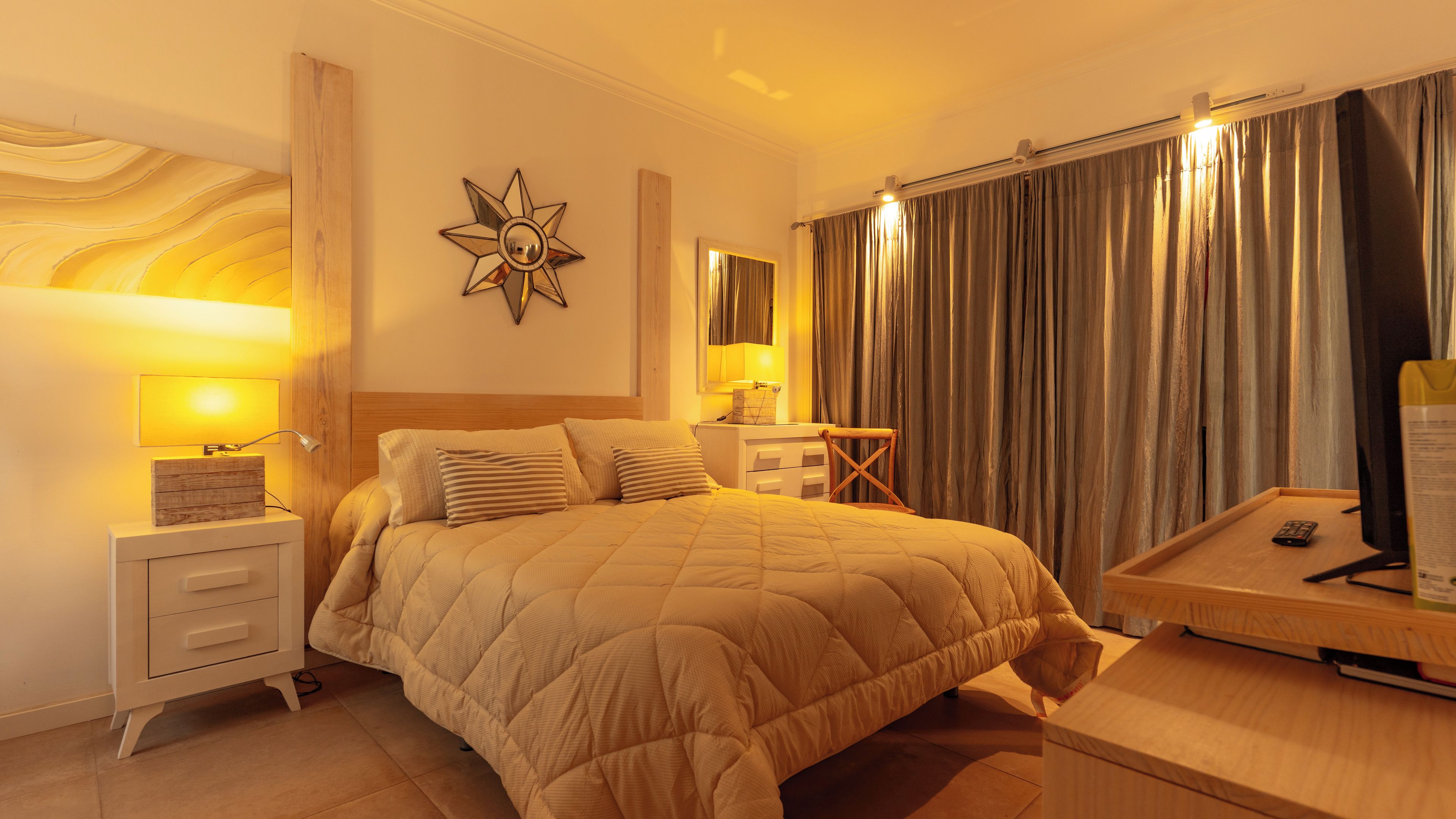 A hotel room with a large bed, bedside tables, a desk, and a mirror.
