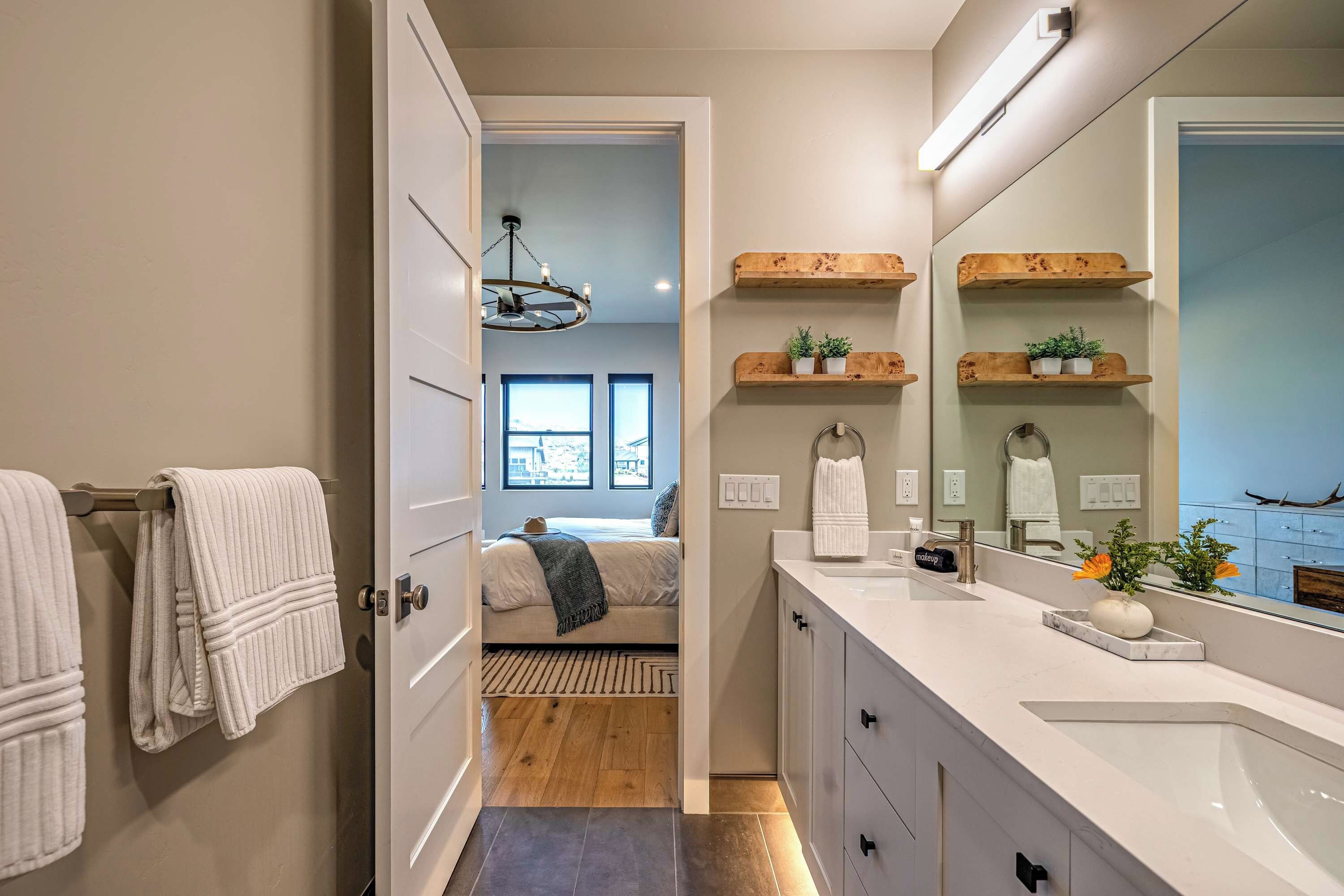 Une salle de bain moderne avec un grand miroir, des étagères en bois et une vue sur une chambre à coucher par une porte ouverte.