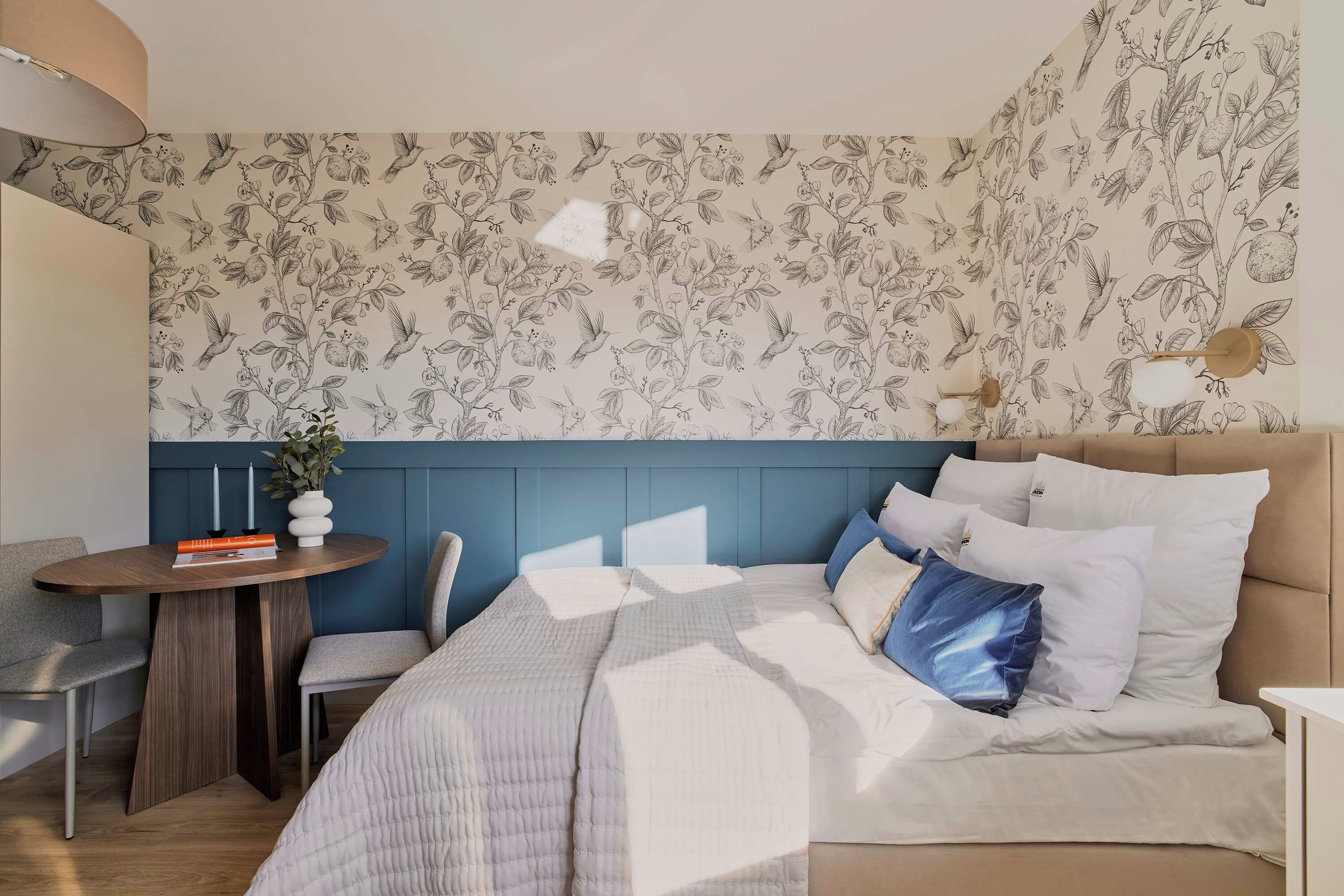 A bedroom with a bed, bedside table, chair, and a wall with a floral pattern.