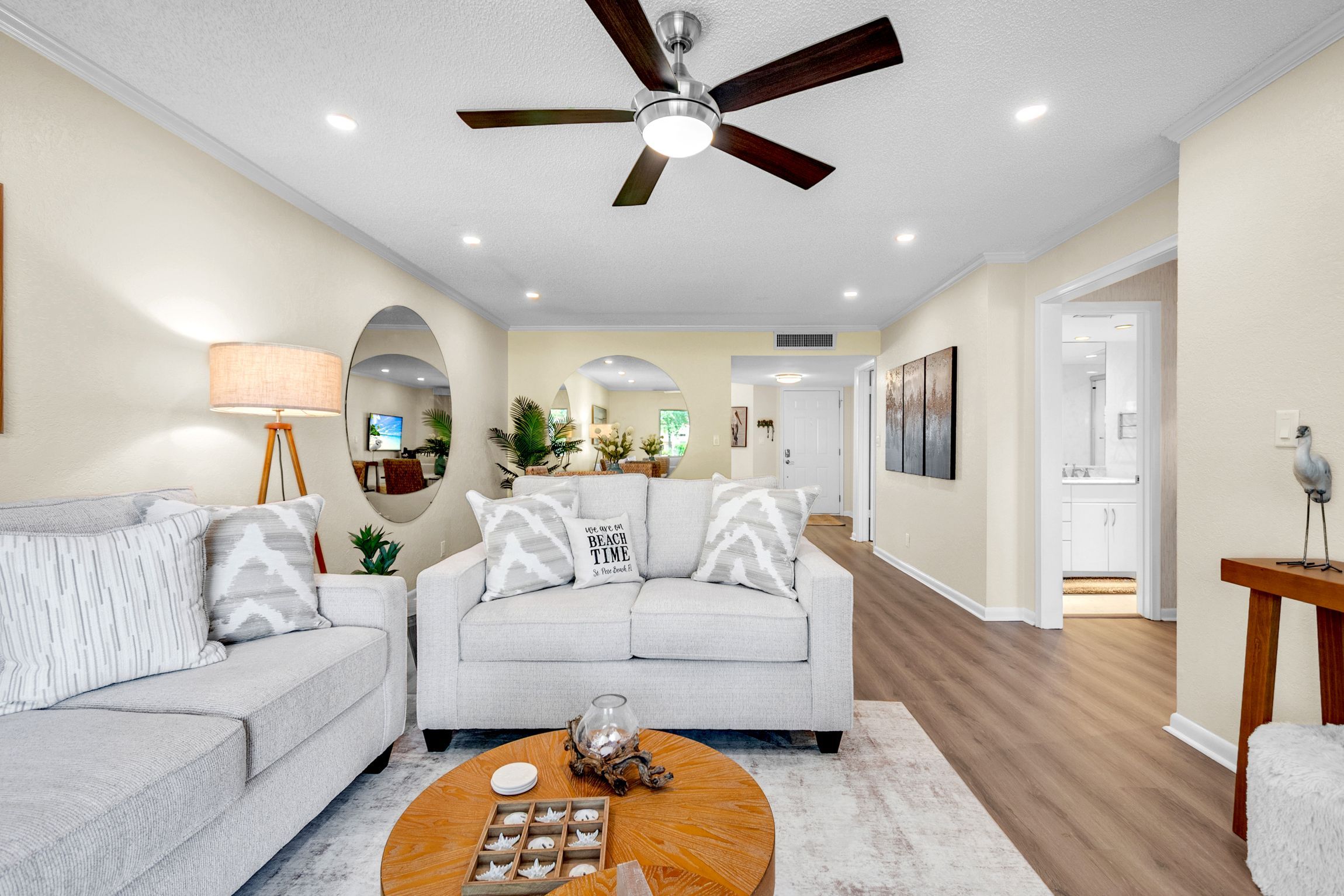 A living room with a ceiling fan, two sofas, a coffee table, and a hallway leading to other rooms.