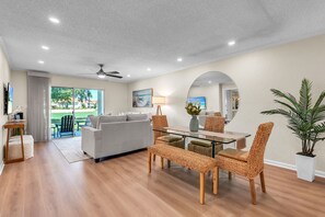 A modern living room with a glass dining table, wicker chairs, a grey sofa, and a ceiling fan. - Ground Floor | Resort Amenities | Minutes to Beaches | Vista Verde East 105 (Saint Petersburg)