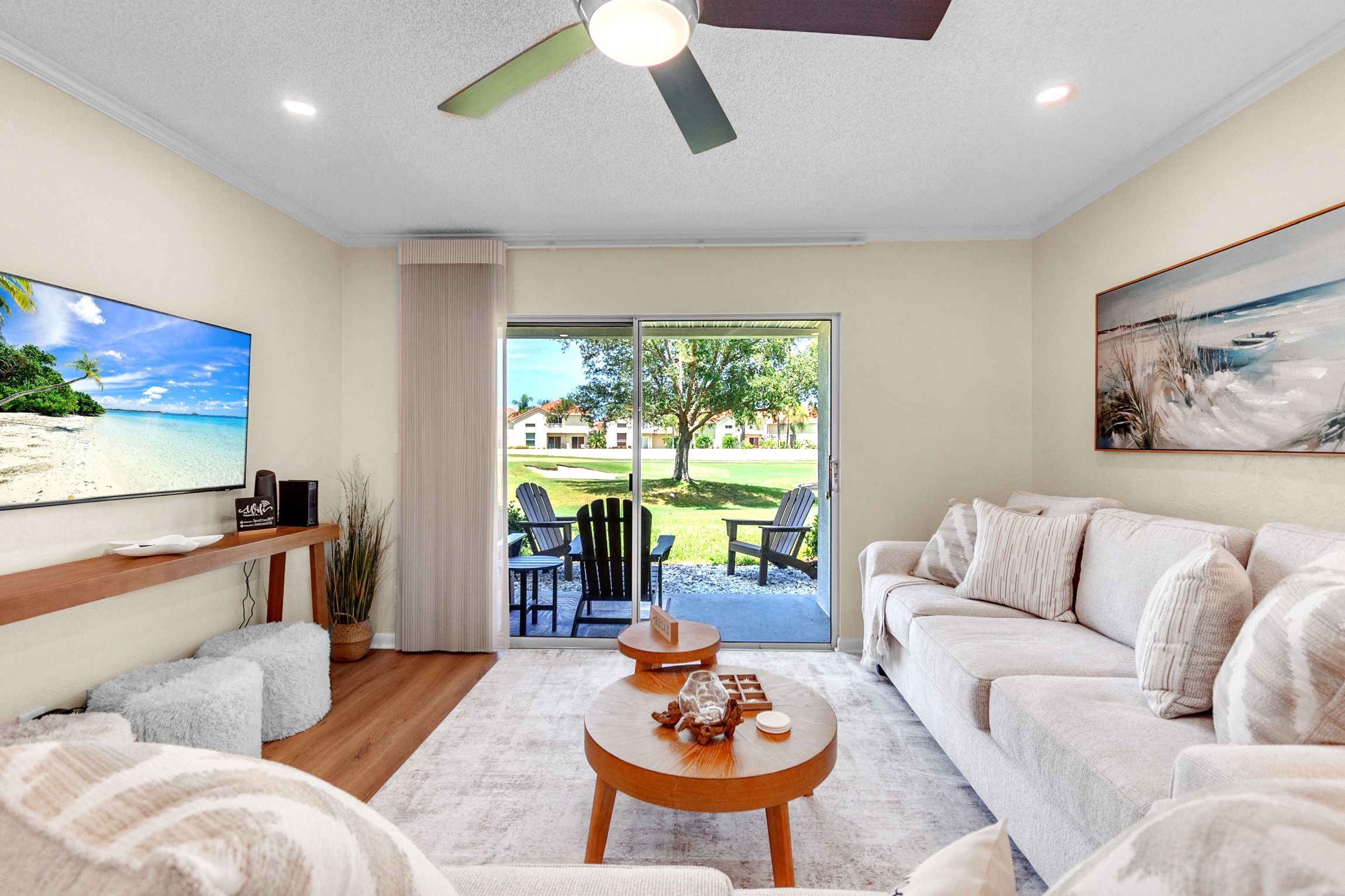 Ein modernes Wohnzimmer mit einem großen Flachbildfernseher, einer Couch, einem Couchtisch und Blick auf einen Golfplatz durch eine Schiebetür.
