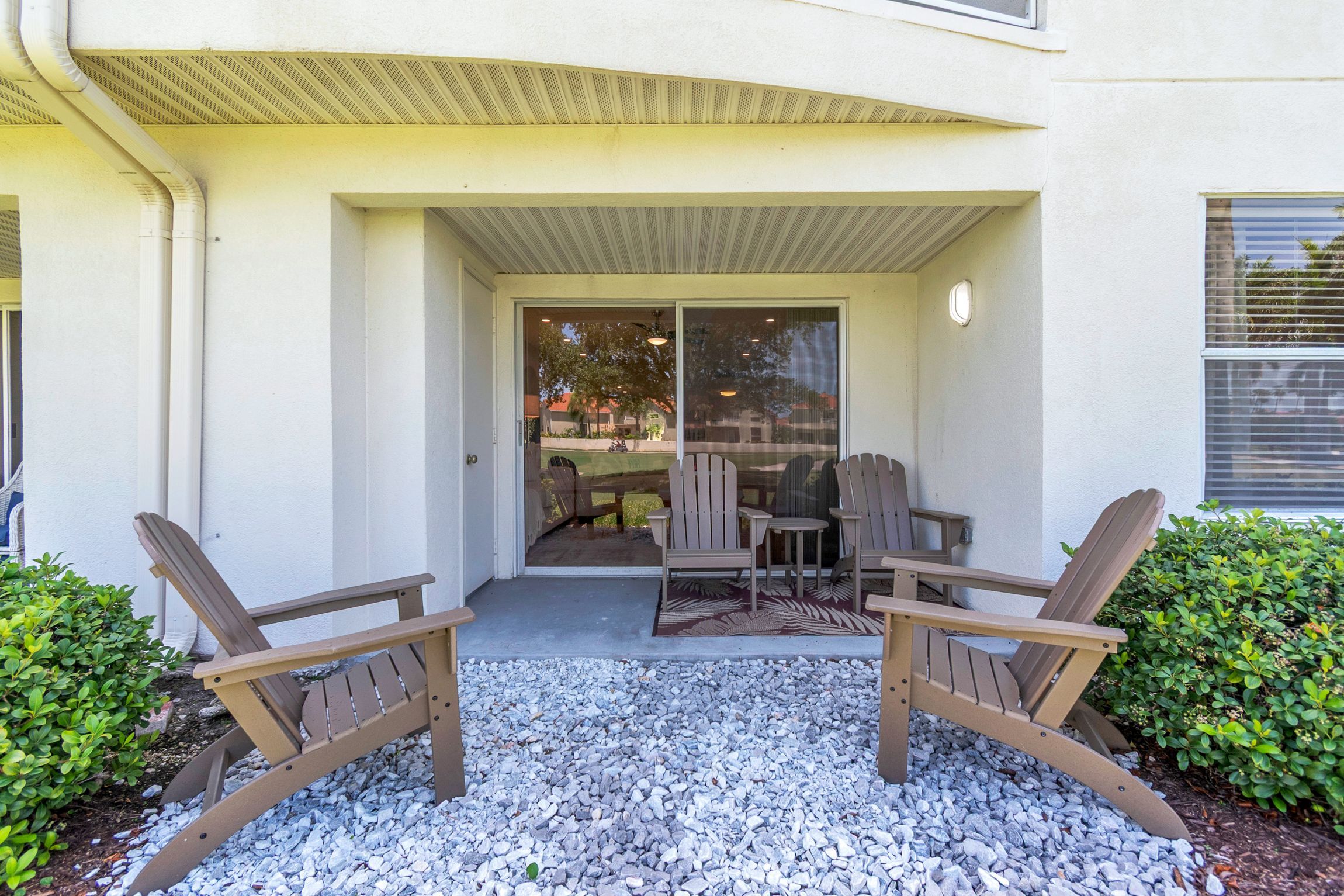 A covered patio area with Adirondack chairs and a table, a sliding glass door leading to a backyard, and a small window with blinds.