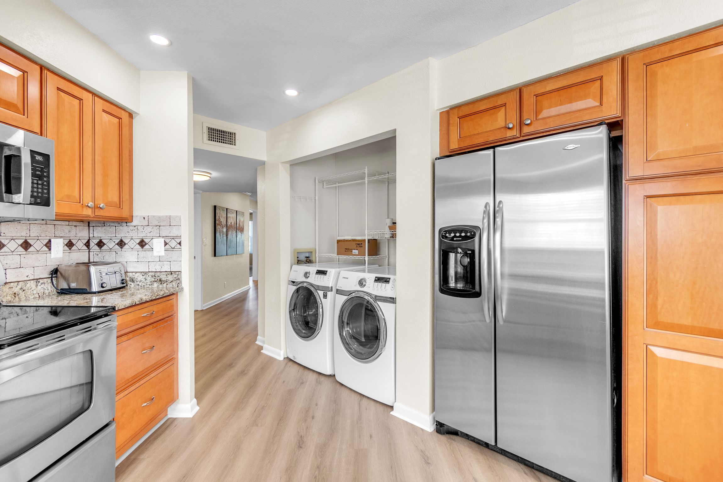 A modern kitchen with stainless steel appliances, wooden cabinets, and a tiled backsplash.