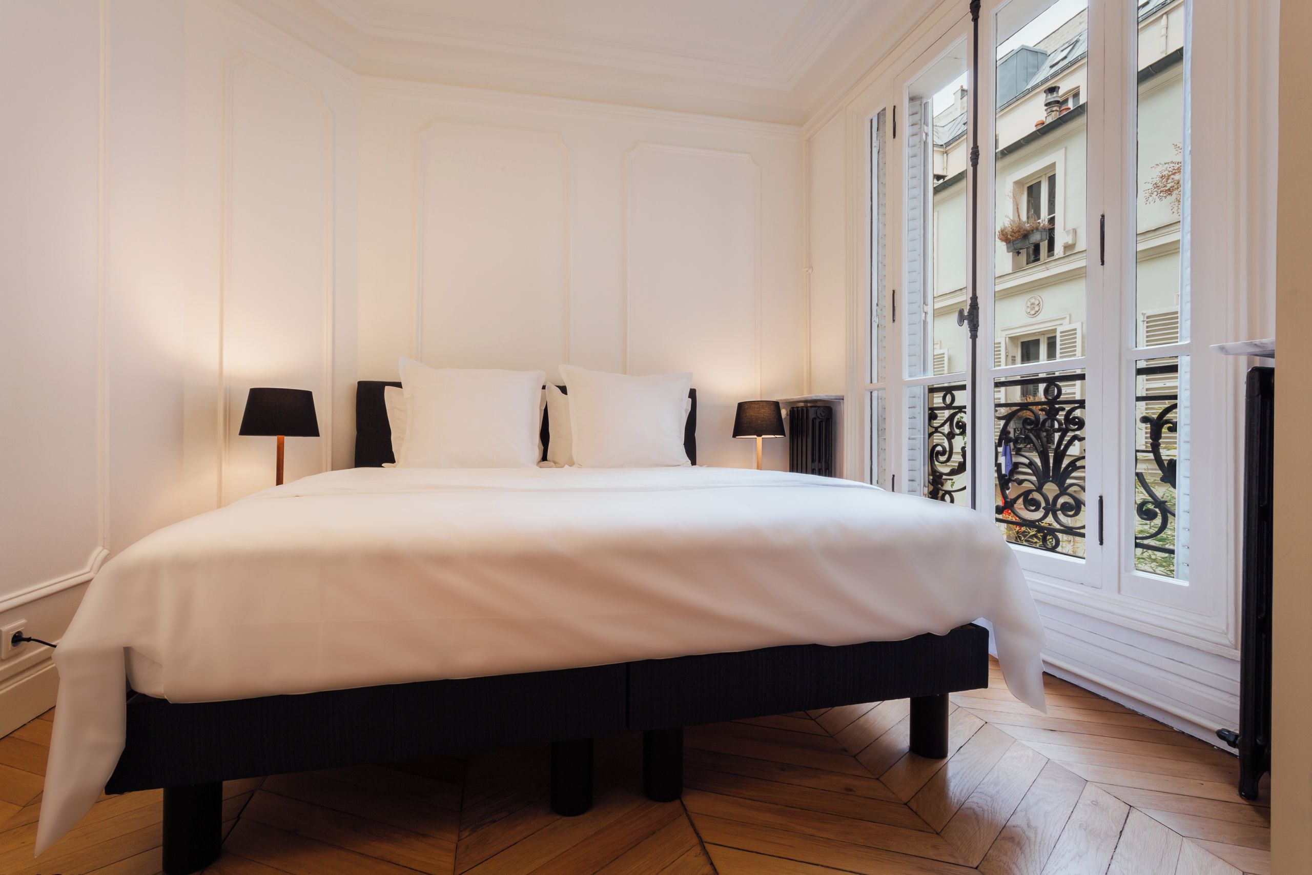 Een hotelkamer met een groot bed, twee nachtlampjes en uitzicht op de stad door een raam.