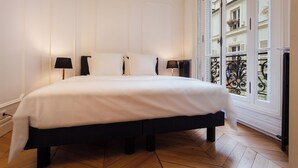 Quarto de hotel com uma cama grande, duas luminárias de cabeceira e vista para a cidade pela janela.