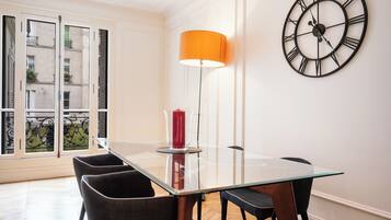 A dining area with a glass table, black chairs, a red candle, and a large wall clock.