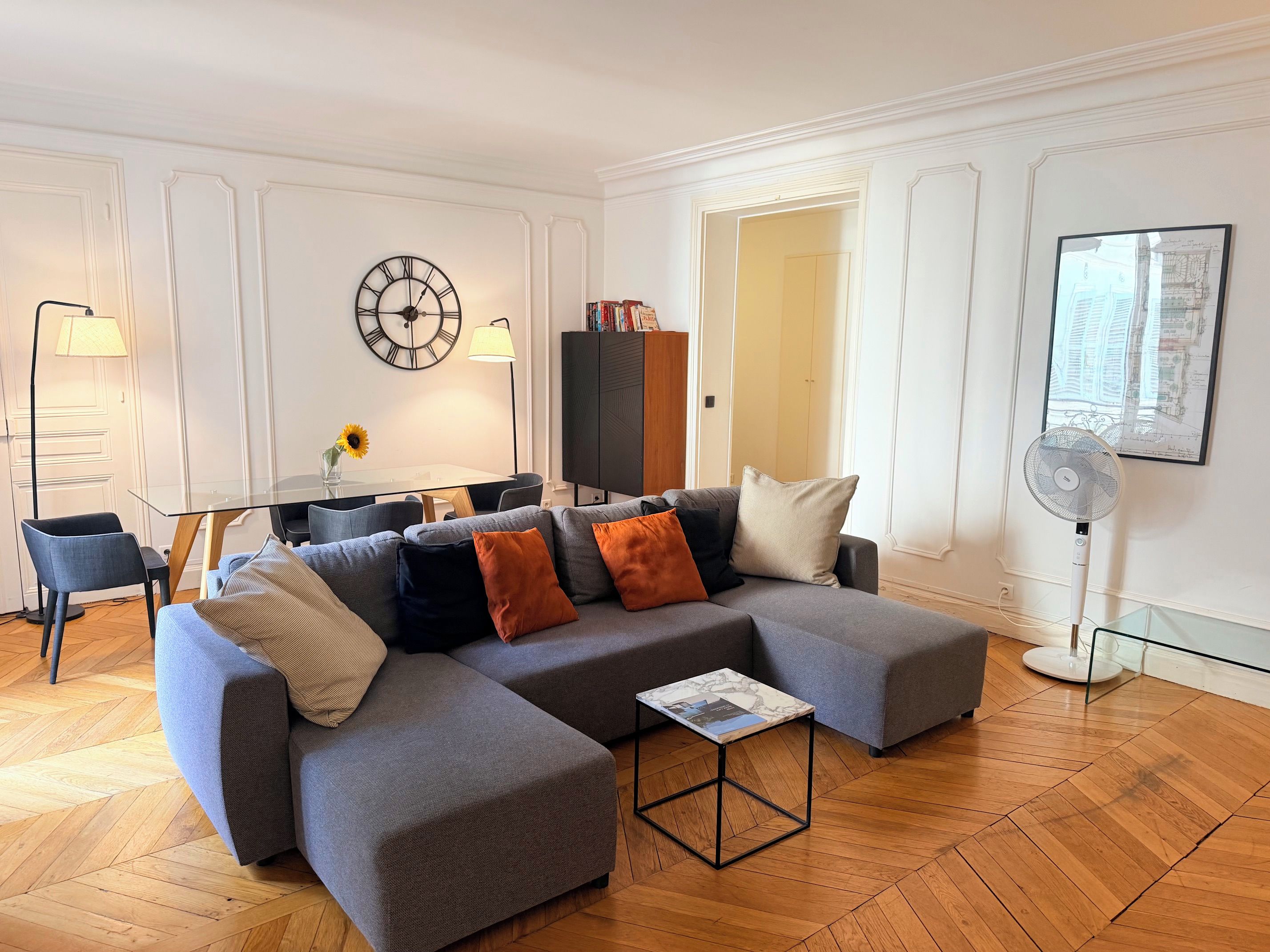 Een moderne woonkamer met een modulaire bank, een glazen salontafel en een eethoek met een tafel en stoelen.