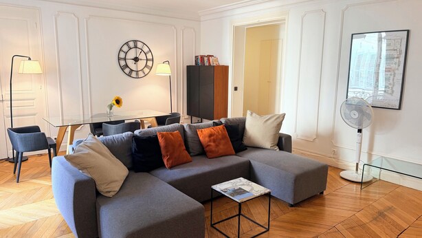Uma sala de estar moderna com um sofá seccional, uma mesa de centro de vidro e um espaço de jantar com mesa e cadeiras.