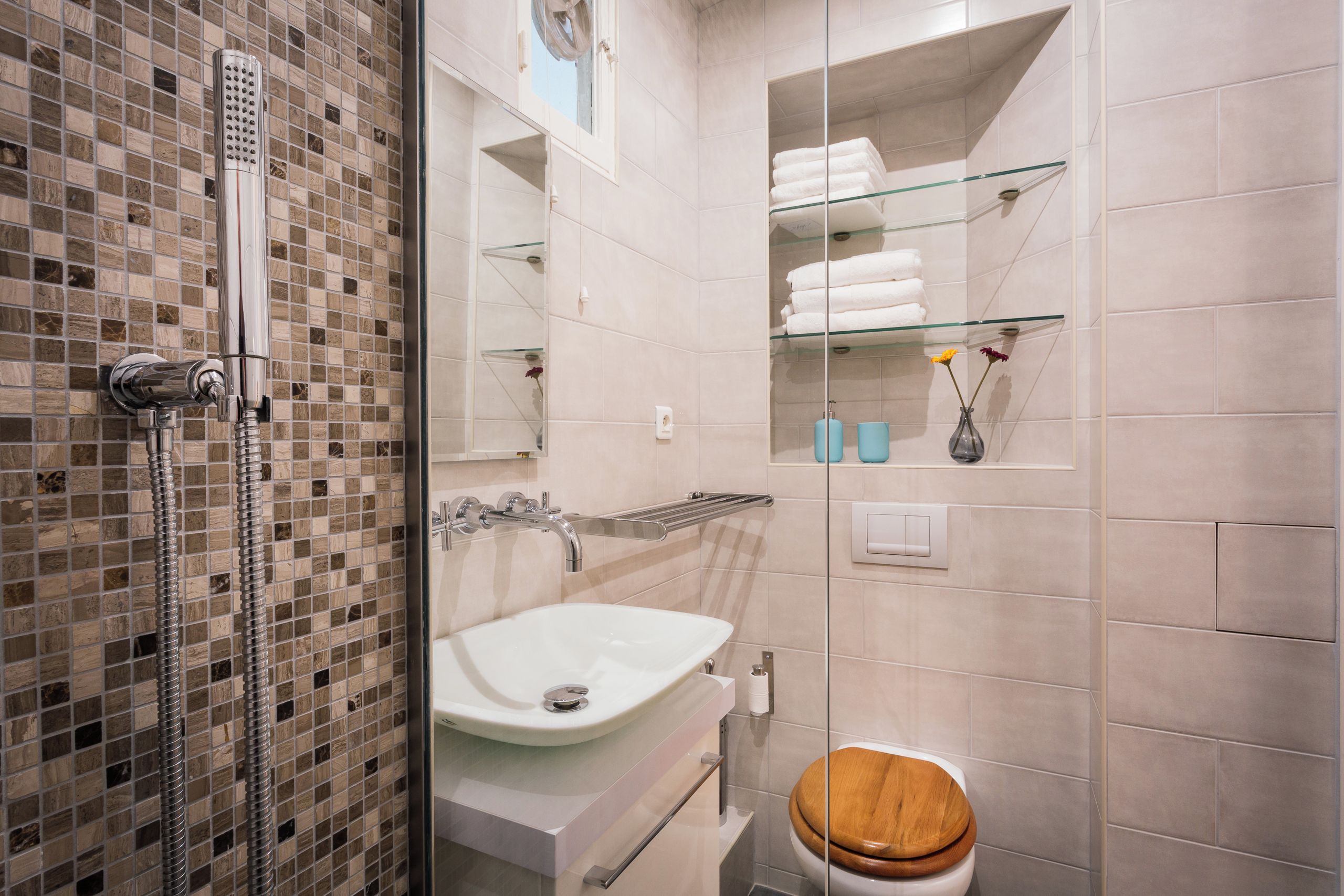 A modern bathroom with a glass shower enclosure, a white sink, and a wooden toilet.