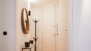 Um corredor com piso de madeira em padrão herringbone, um cabideiro, um espelho e uma porta.
