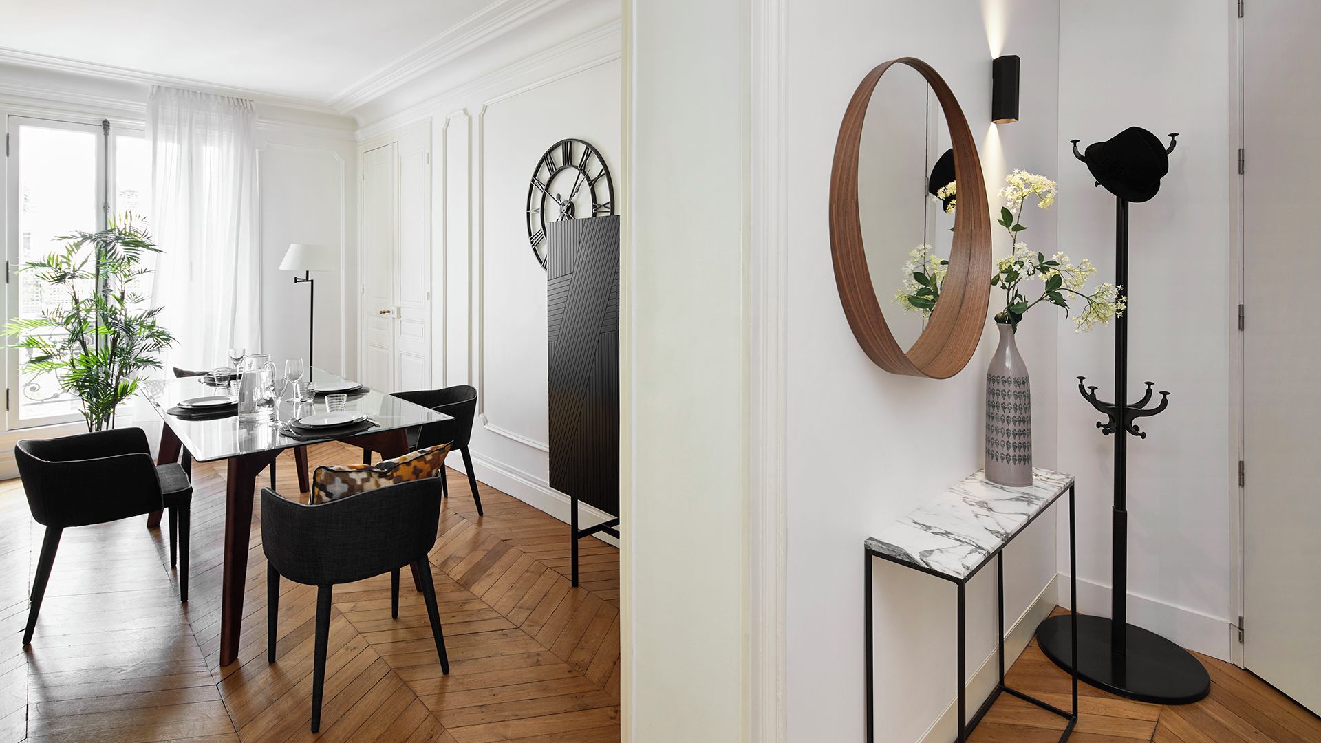 Un coin repas doté d’un parquet en bois disposé en motif à chevrons, d’une table à manger pour quatre personnes et de chaises noires.