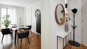 Uma área de refeições com piso de madeira em padrão herringbone, uma mesa para quatro pessoas e cadeiras pretas.