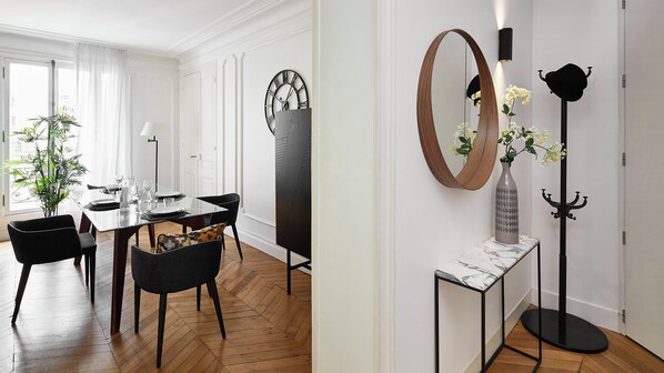 A dining area with a wooden herringbone floor, a dining table set for four, and black chairs.