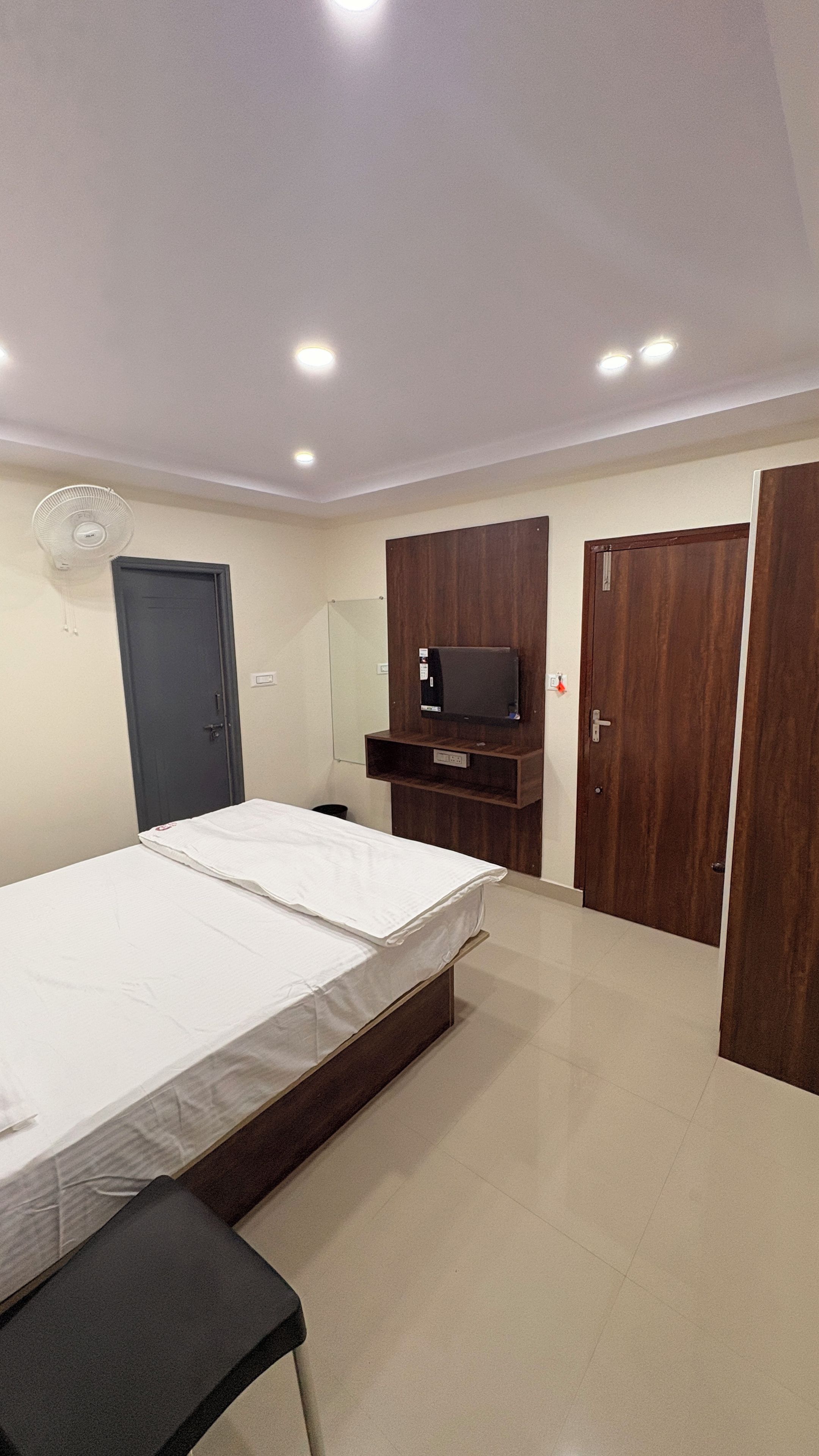 Un dormitorio con una cama, un televisor instalado en un mueble de madera, una puerta y un ventilador de techo.