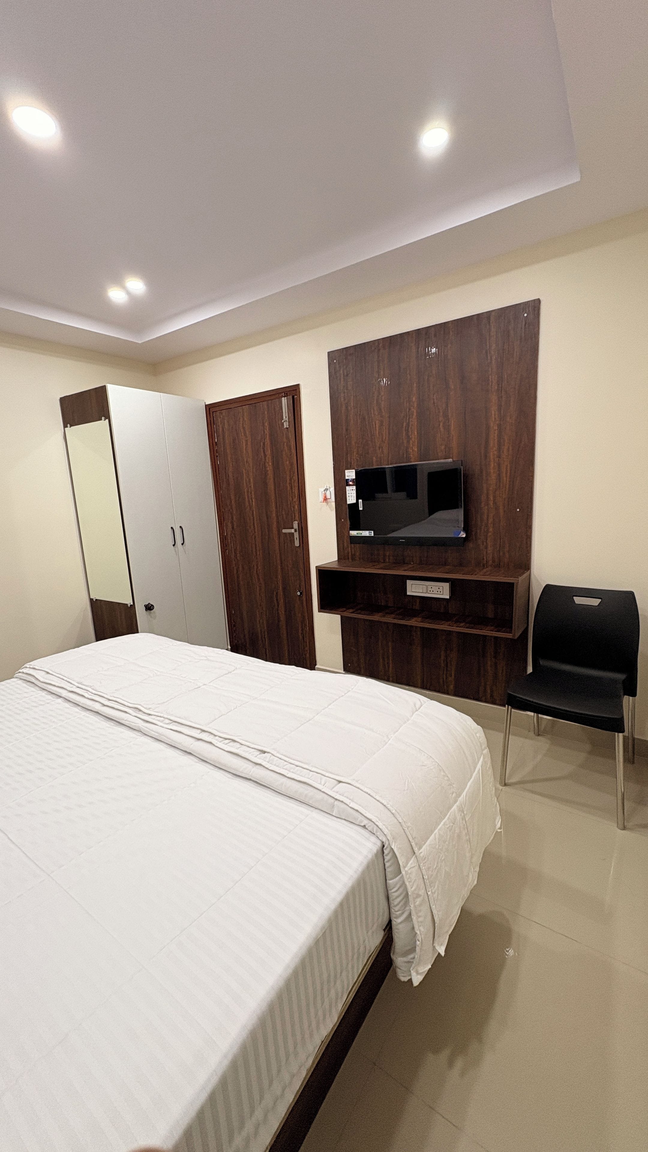 Habitación de hotel con cama, armario, espejo, televisor y escritorio.