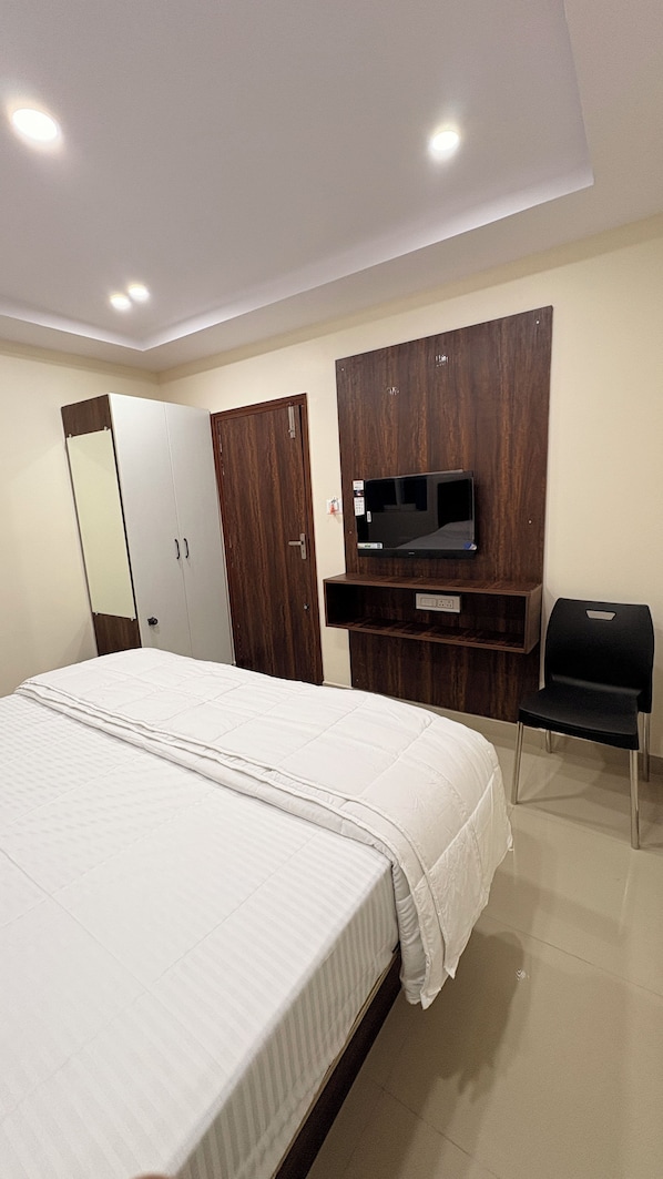 A hotel room with a bed, wardrobe, mirror, television, and a desk.