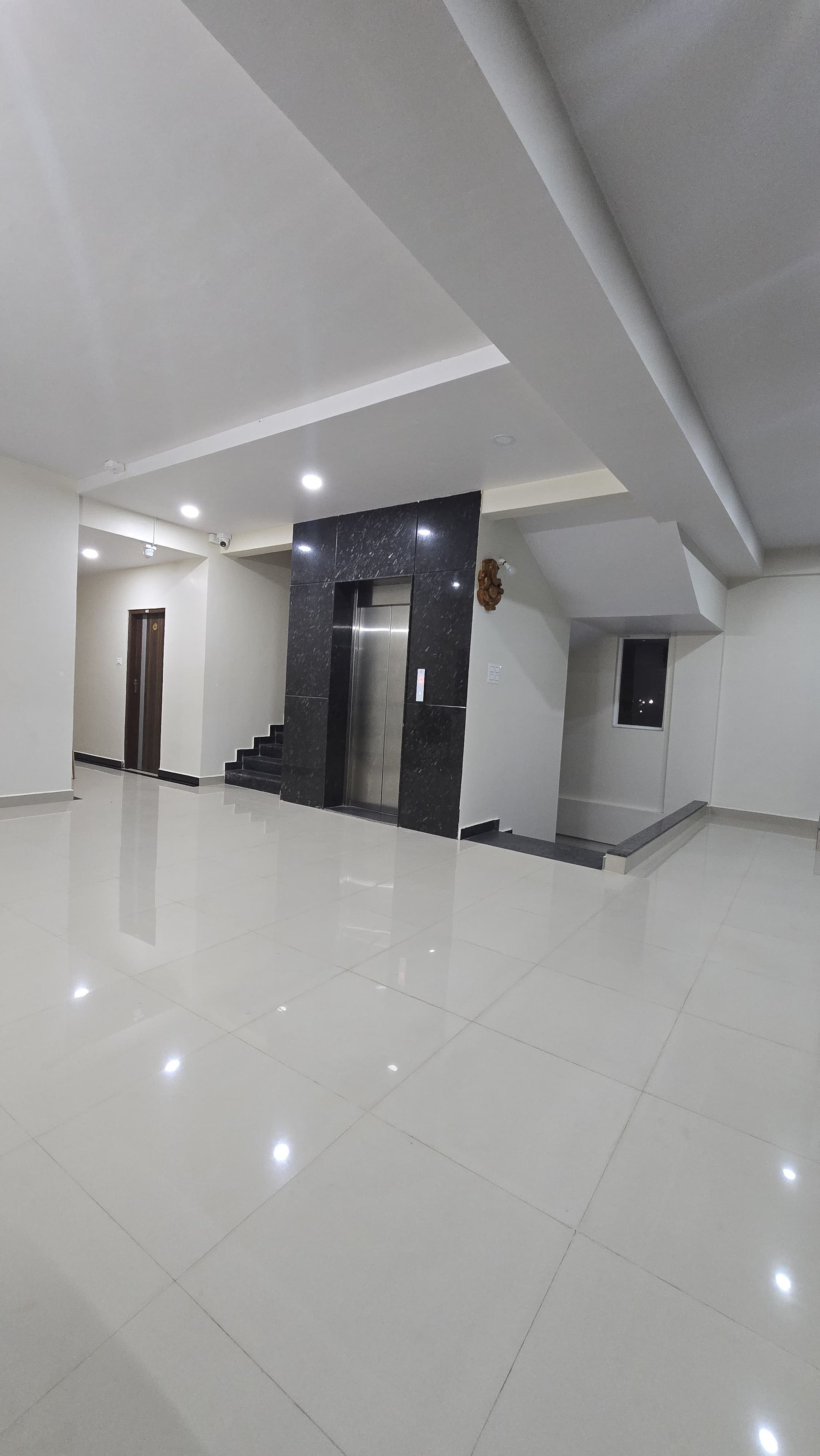 A spacious, modern interior with a polished floor, a central elevator, and a staircase leading to an upper level.