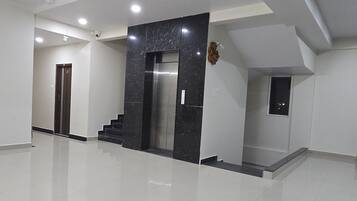 A spacious, modern interior with a polished floor, a central elevator, and a staircase leading to an upper level.