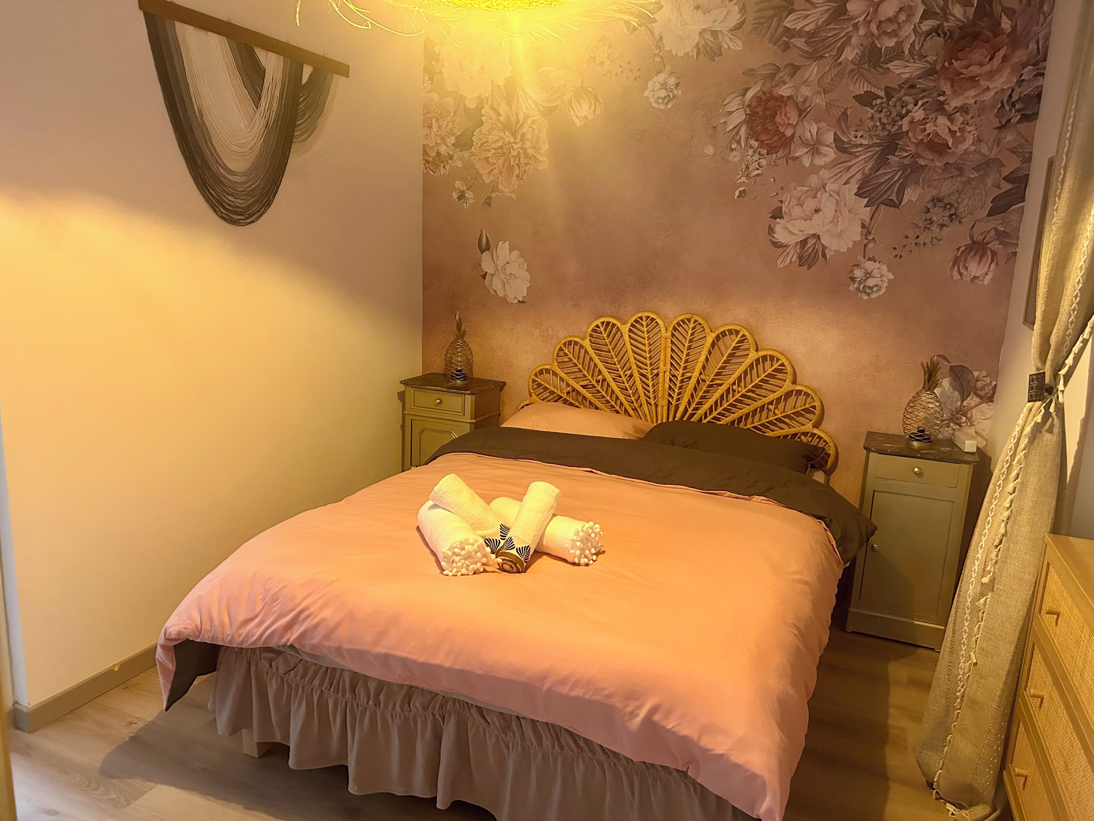 Een slaapkamer met een bed, een nachtkastje, een wandlamp en bloemenbehang.