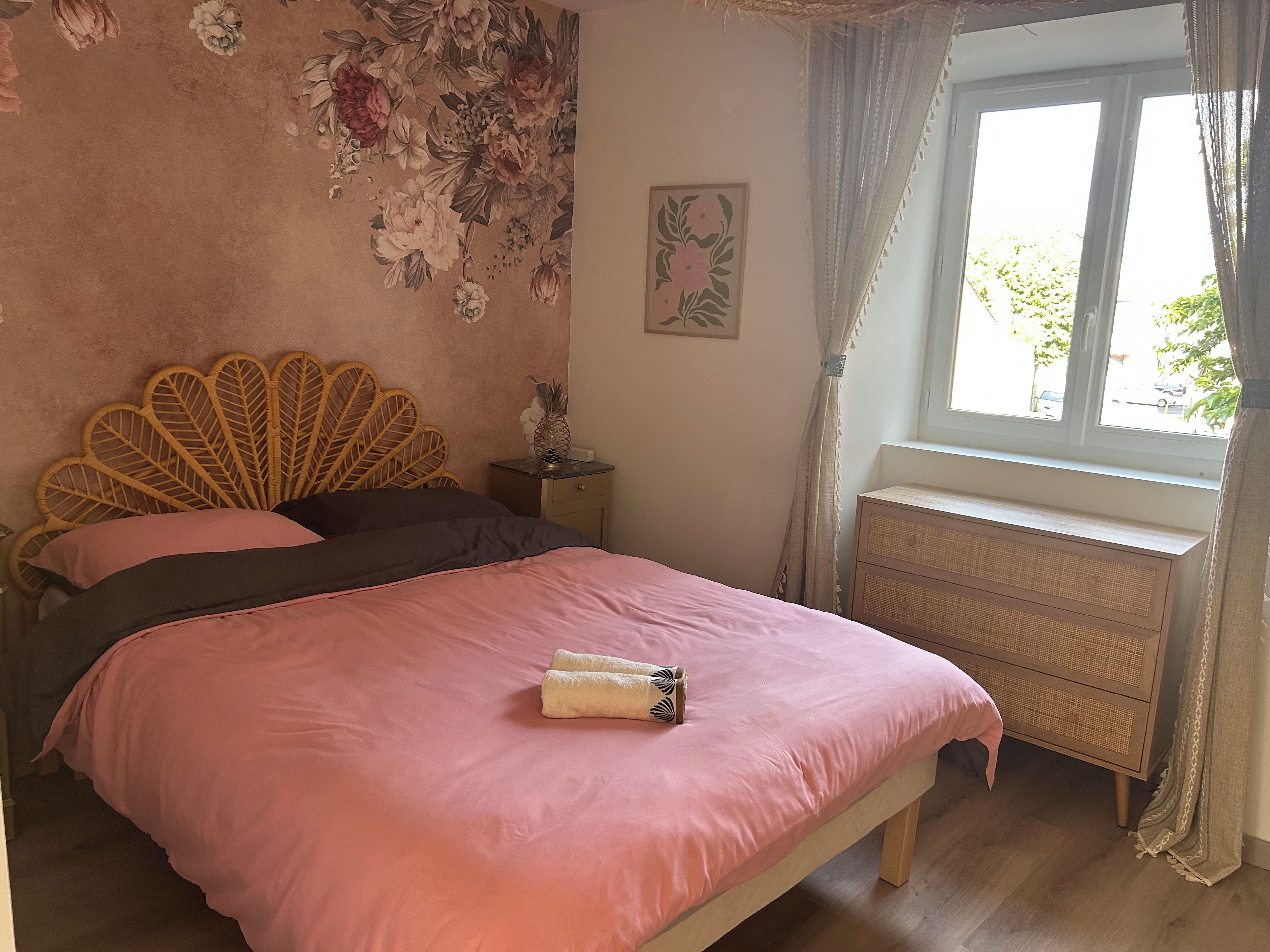 Une chambre à coucher comprenant un lit, une table de chevet, une commode, une fenêtre avec des rideaux et un motif floral décorant le mur.