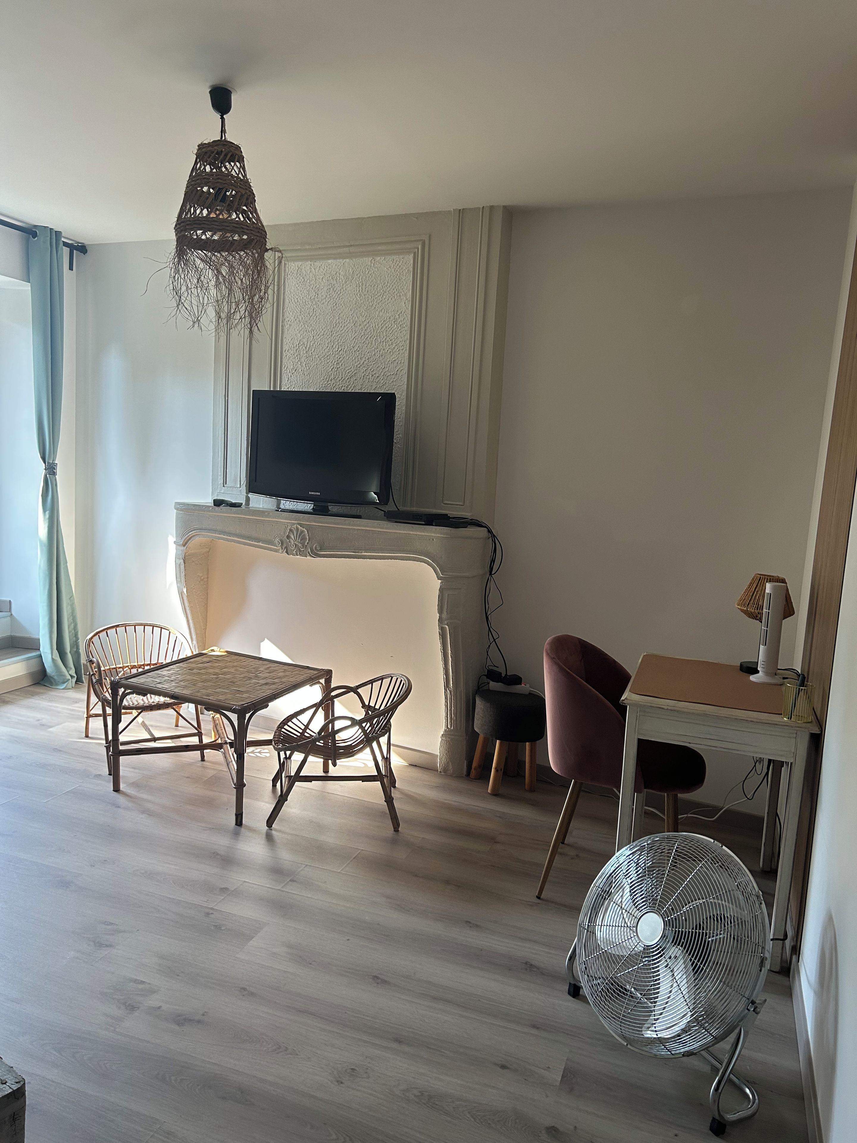 Een woonkamer met een televisie, rieten meubels, een ventilator en een tafel met een lamp.