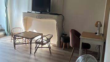 Een woonkamer met een televisie, rieten meubels, een ventilator en een tafel met een lamp.