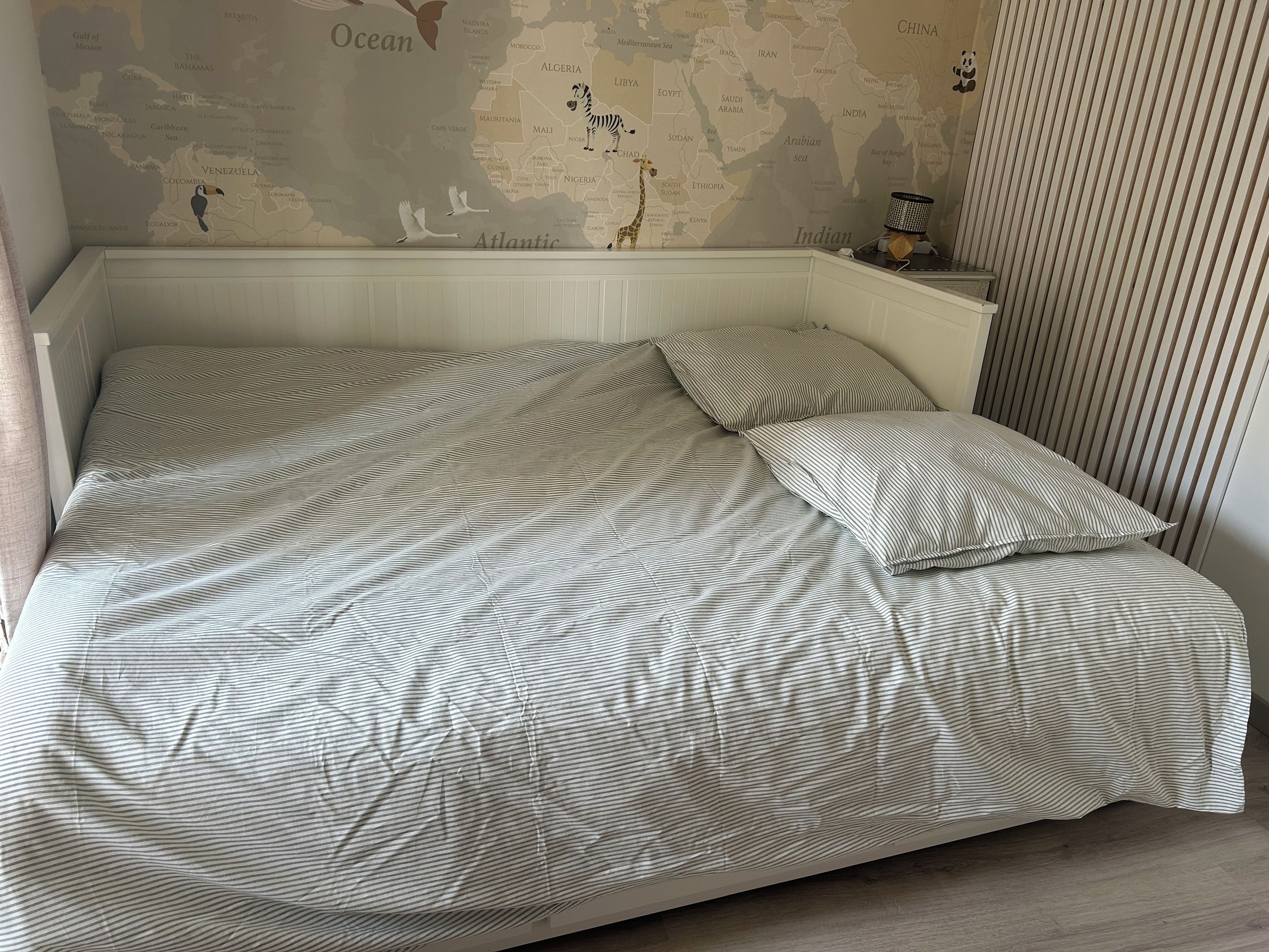 Un lit avec une literie à rayures dans une pièce où est accrochée une carte du monde au mur.