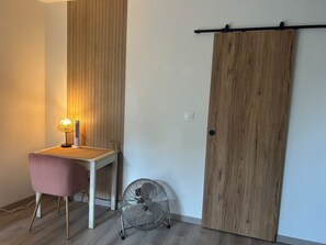 A room with a desk, a chair, a standing fan, and a sliding door.
