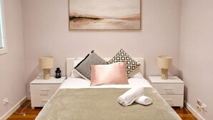 Un dormitorio con una cama, dos mesitas de noche, una lámpara de noche, un cuadro en la pared y una ventana.