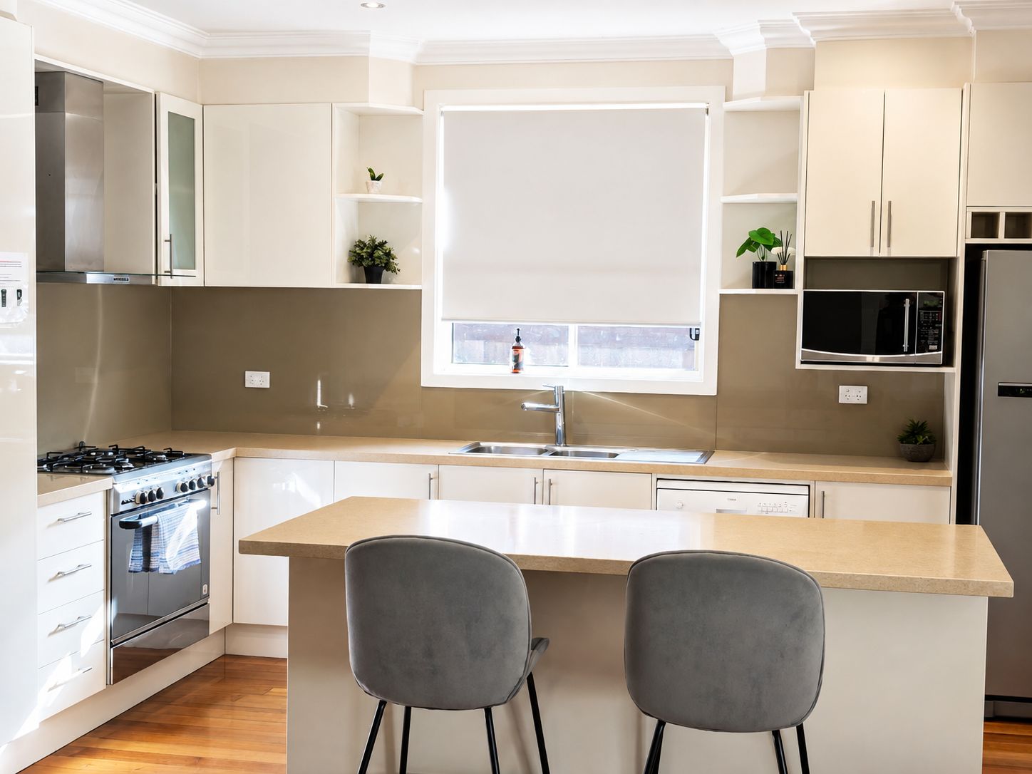 A modern kitchen with a central island, two bar stools, a stainless steel stove, and a microwave.
