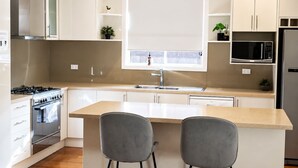 Una cocina moderna con una isla central, dos taburetes de bar, una estufa de acero inoxidable y un microondas.