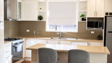 A modern kitchen with a central island, two bar stools, a stainless steel stove, and a microwave.