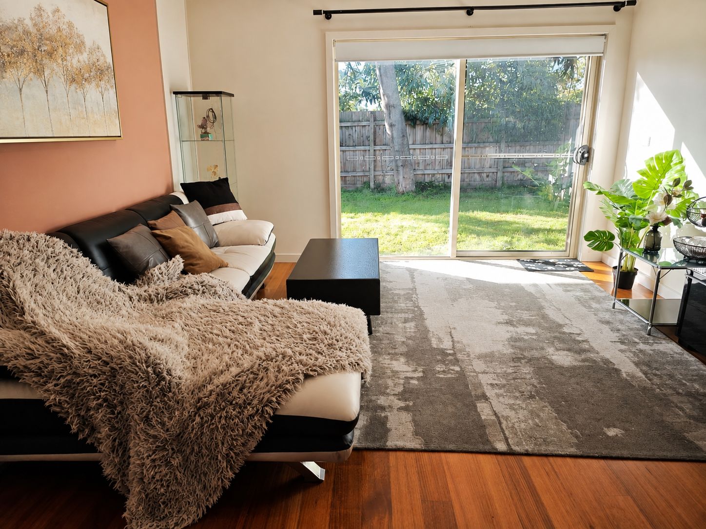 A living room with a sofa, a coffee table, a glass cabinet, and a sliding glass door leading to a backyard.