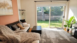 Una sala de estar con un sofá, una mesa de centro, un aparador de vidrio y un ventanal corredizo que da a un patio trasero.