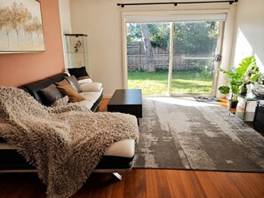 A living room with a sofa, a coffee table, a glass cabinet, and a sliding glass door leading to a backyard. - Charming 3BR Home with Free Parking in Nunawading (Nunawading)