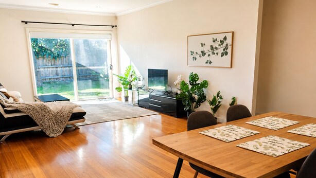 Una sala moderna con un sofá, una mesa de comedor con sillas, un televisor y un ventanal con vistas a un jardín trasero.