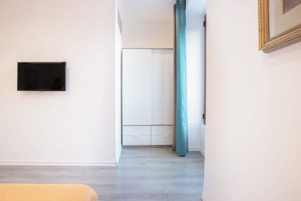 Habitació amb televisió de pantalla plana penjada a la paret, un pilar de color turquesa i una porta blanca que condueix a una altra habitació.
