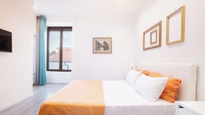 Une chambre d’hôtel avec un lit, une télévision, une fenêtre avec des rideaux et un tableau encadré au mur.