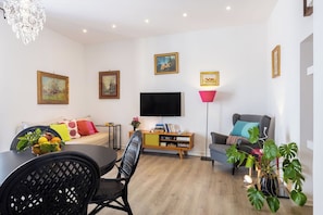 A modern living room with a sofa, a dining table with chairs, a flat-screen TV, a floor lamp, and a potted plant. - Casa Mirea – Downtown Sorrento, Between the Cathedral and Marina Piccola (Sorrento)