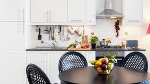 Une cuisine moderne avec des armoires blanches, une hotte en acier inoxydable et un coin repas comprenant une table ronde et des chaises.