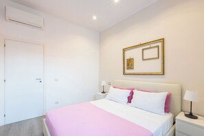Una habitació d'hotel amb un llit, taules de nit, una porta i un quadre penjat a la paret.