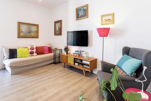 A living room with a sofa, a TV, a bookshelf, and a floor lamp. - Casa Mirea – Downtown Sorrento, Between the Cathedral and Marina Piccola (Sorrento)