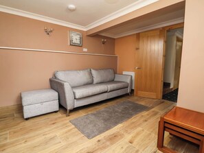 Ein Wohnzimmer mit grauem Sofa, einem kleinen Tisch, einem grauen Teppich und einer Holztür.